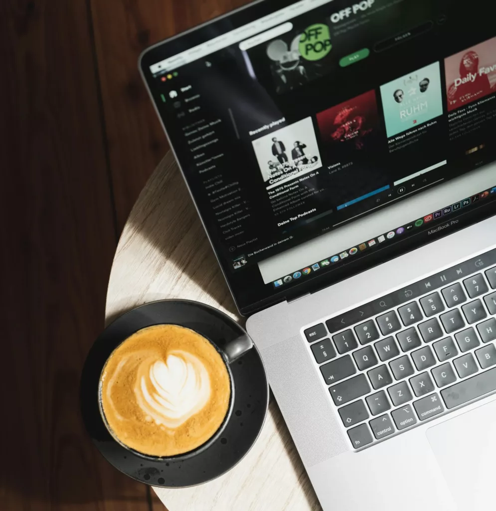 A LAPTOP SCEEN SHOWING APPLE PODCASTS PAGE AND COFFEE ON A SMALL TABLE.