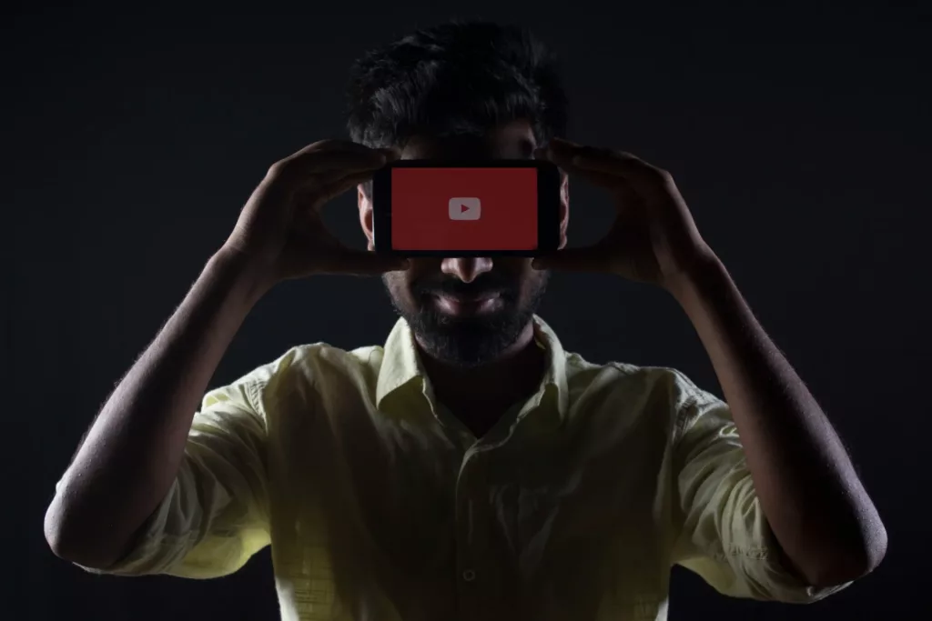 MAN HOLDING PHONE DISPLAYING YOUTUBE LOGO INFRONT OF HIS HEAD