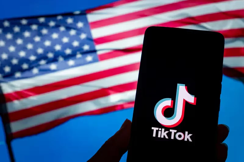 USA Flag behind a smartphone displaying TikTok Logo